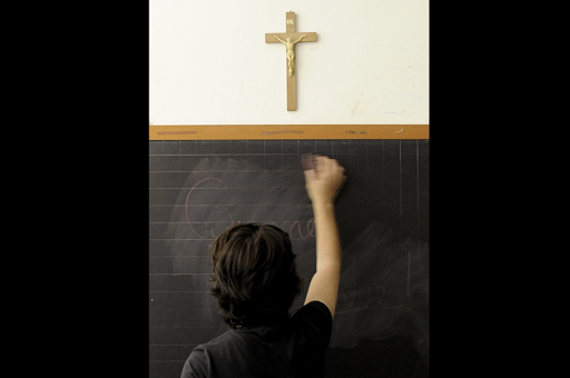 ITALY, Viterbo : A teacher writes on the blackboard under a crucifix in a classroom &#8211; it