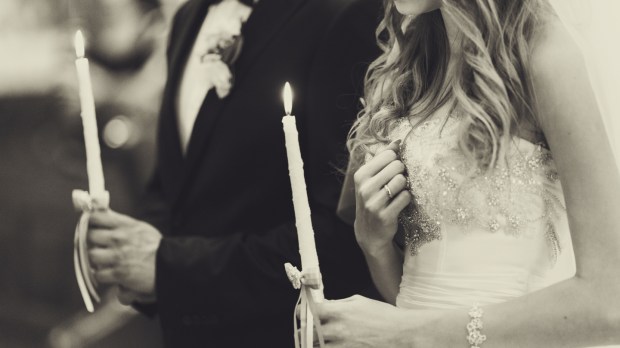 A wedding couple pray holding burning candles in their arms