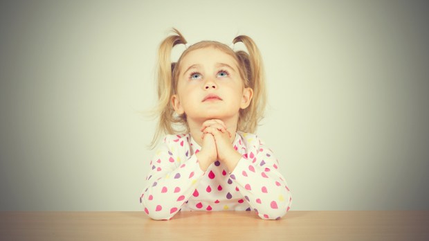 Little girl praying and looking up. Sitting at the table.