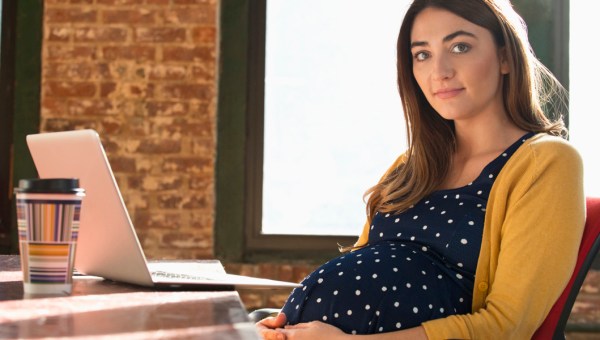 Młoda pracująca kobieta w ciąży siedzi w swoim biurze