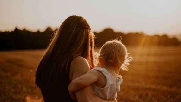 back view photo of a woman in black sleeveless top carrying a toddler