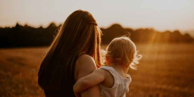 back view photo of a woman in black sleeveless top carrying a toddler