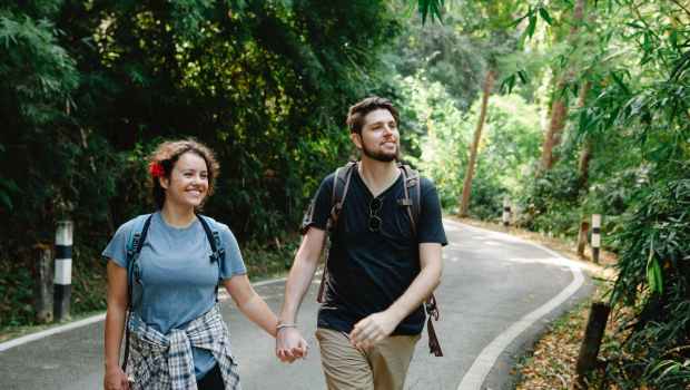 delighted couple holding hands while strolling on road in tropical park