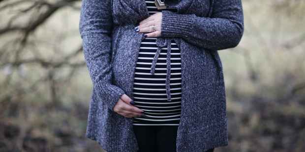 woman pregnant in black and white striped shirt standing near bare tree