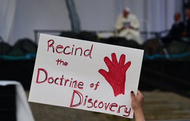 A-person-holds-a-protest-sign-reading-Recind-the-Doctrine-of-Discovery-at-Nakasuk-Elementary-School-Square-in-Iqaluit-AFP