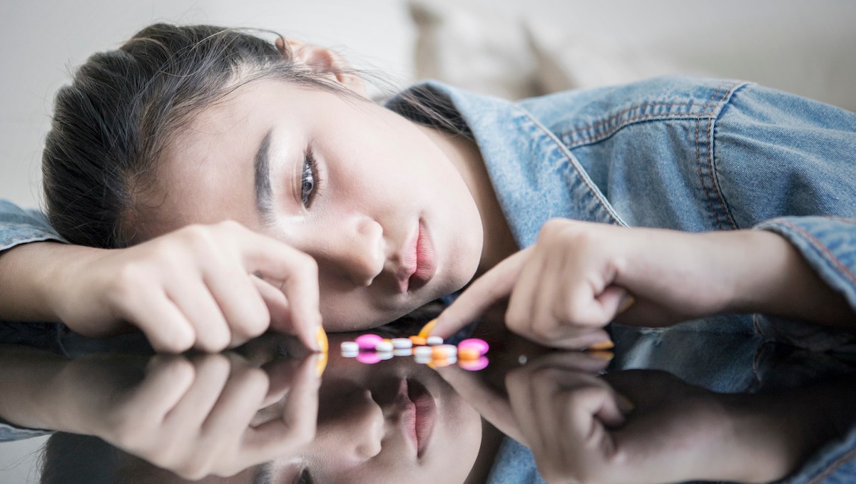 Picture of teenage girl looks sad while counting drugs on the table at home