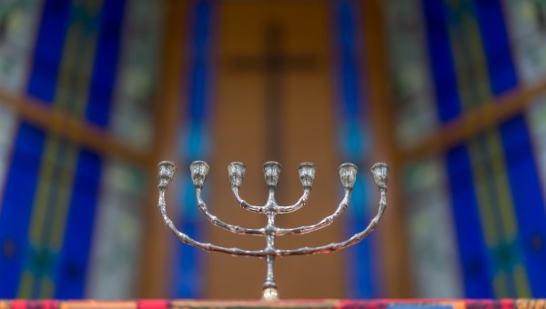 menora stojąca na ołtarzu kościoła z krzyżem na ścianie w tle